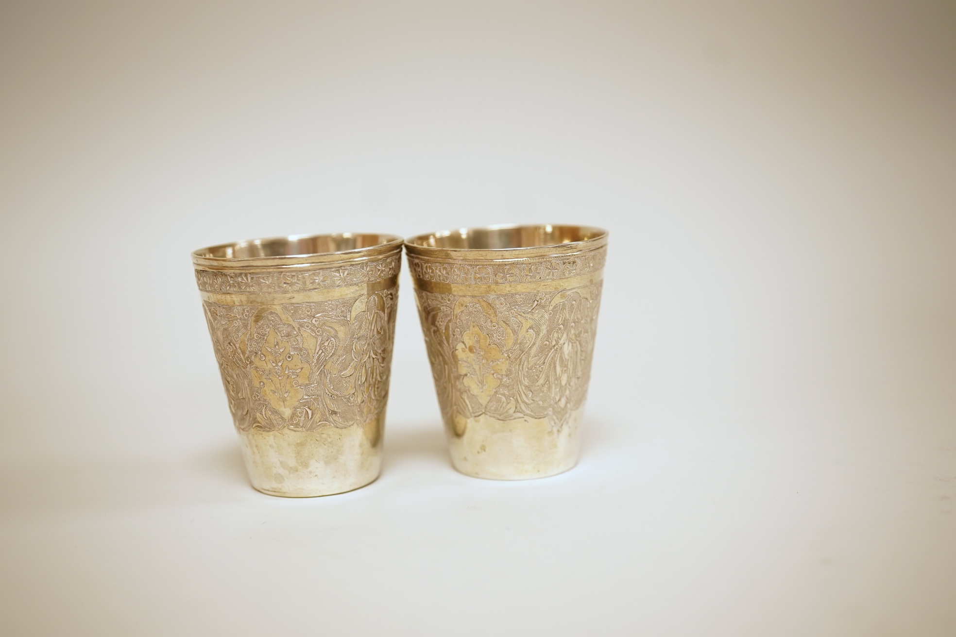 A set of six 20th century Middle Eastern white metal tots, 42mm and matching tray, 25.2cm, all engraved with geometric foliate decoration.